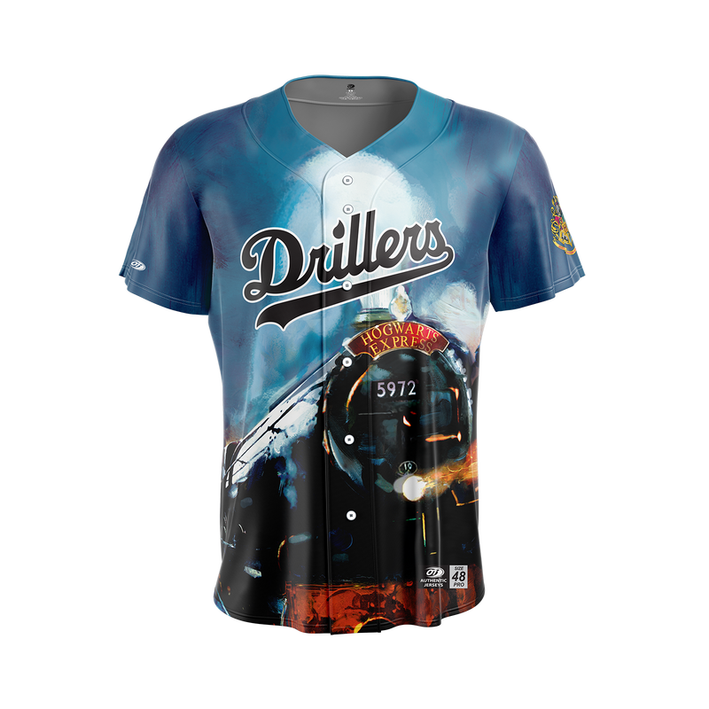 A short-sleeve baseball-style jersey with a blue gradient background and a large printed graphic of a black steam locomotive. The word "Drillers" appears across the chest in stylized lettering, with additional graphic text and small logos near the lower front.